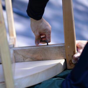 Close-up of a person assembling wooden furniture with an Allen wrench on a sunny day.